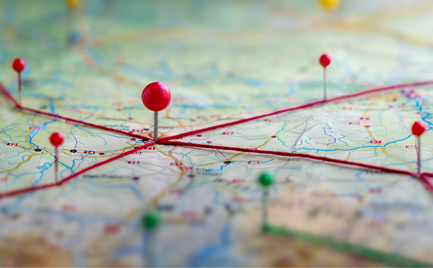 A close-up view of a map with red lines marking roads and various colored pins indicating different locations