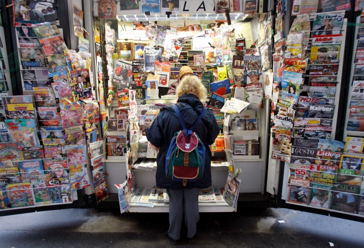 A woman facing away from the camera looks at a large display of magazines and newspapers.