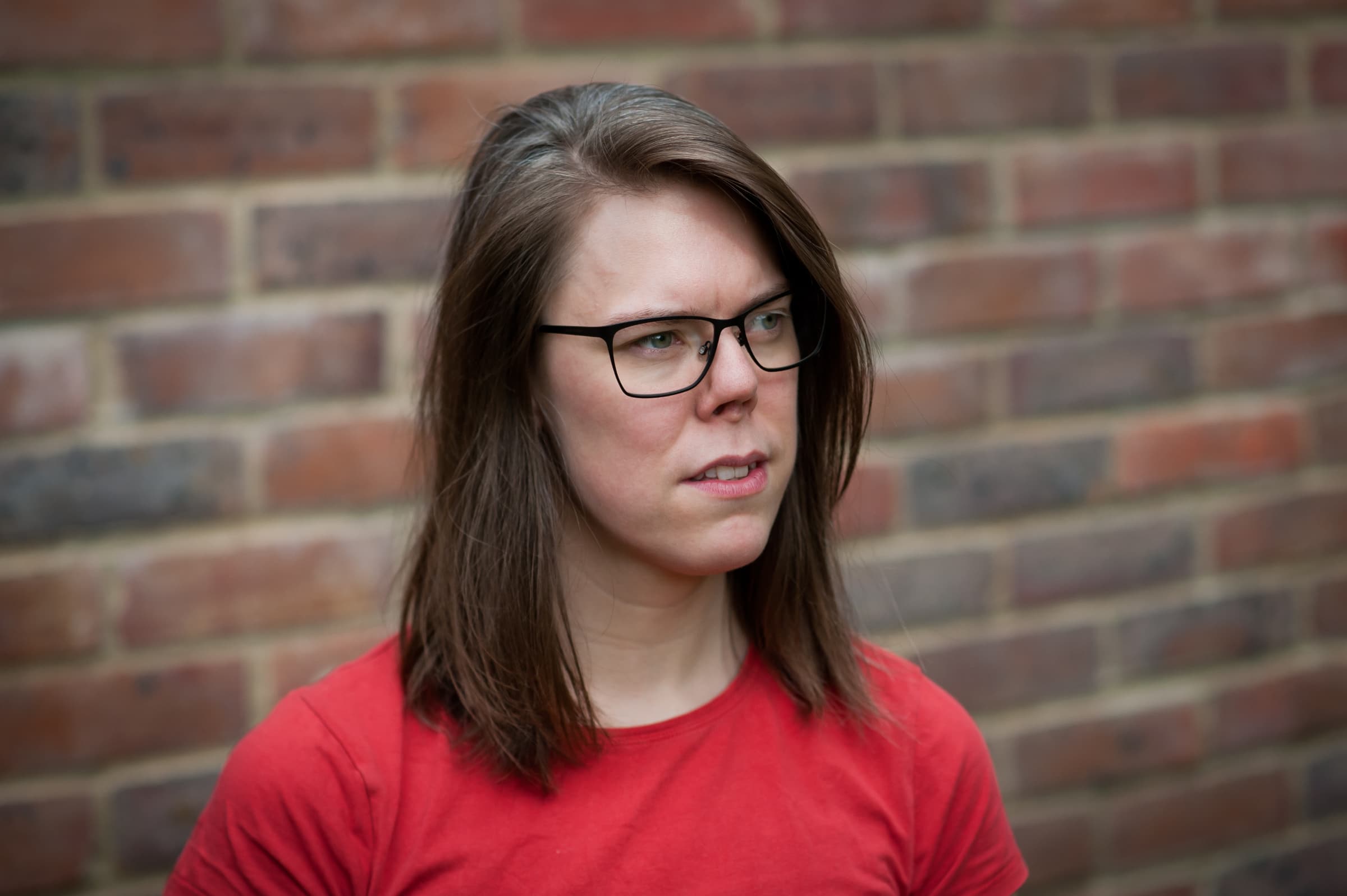 Photo of Issy Long against a brick wall, looking into the distance.