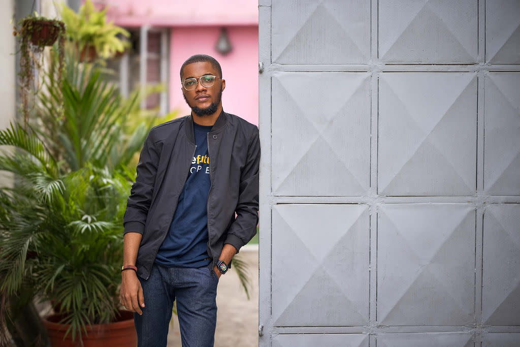 Author Adewale in a plant-covered courtyard leaning against a large door