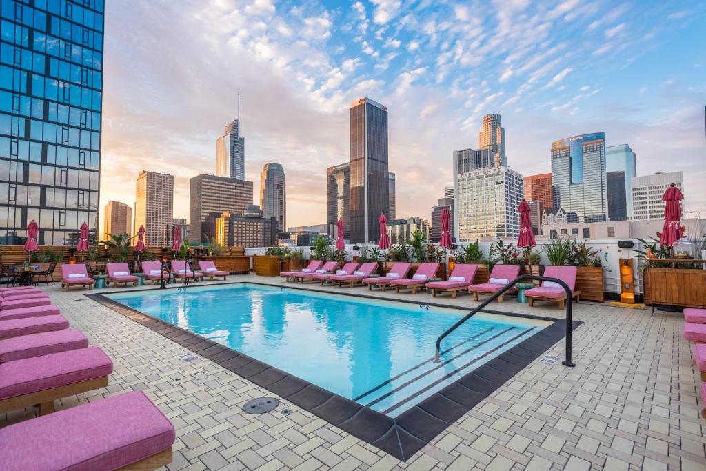 una piscina en la azotea con tumbonas rosas y vistas al perfil urbano en Freehand Los Angeles, en Los Ángeles