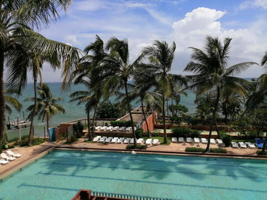 uma piscina com palmeiras e o oceano ao fundo em Hotel Jardin Savana Dakar em Dakar