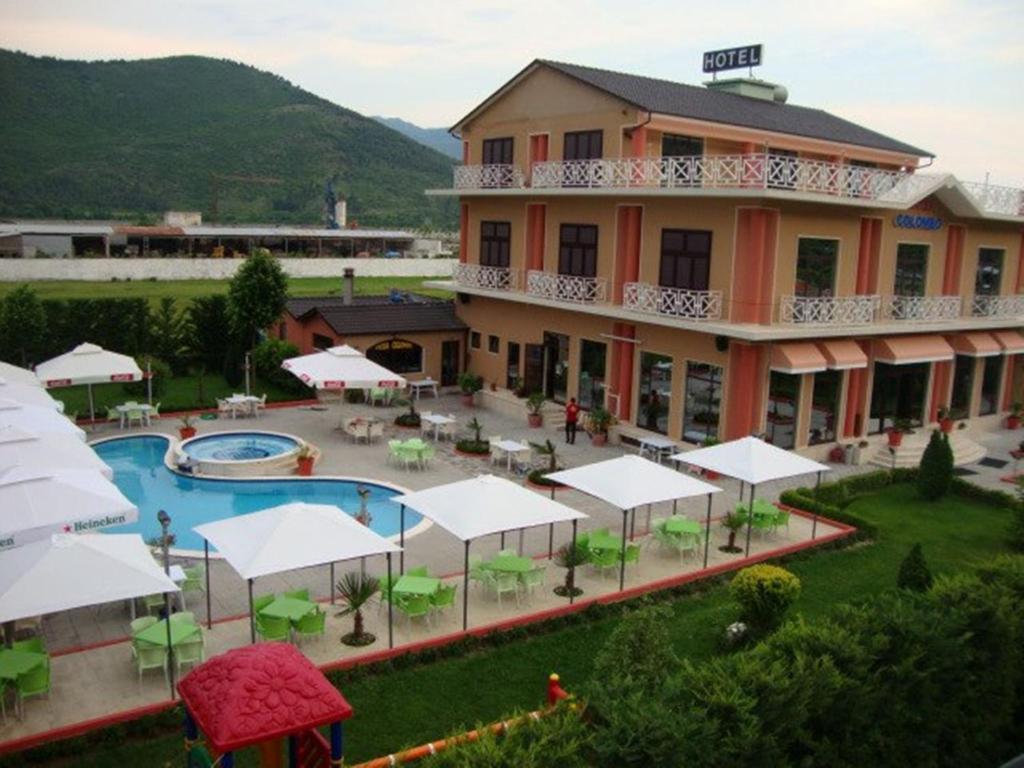 un grande edificio con piscina, tavoli e ombrelloni bianchi di Hotel Colombo Elbasan a Elbasan