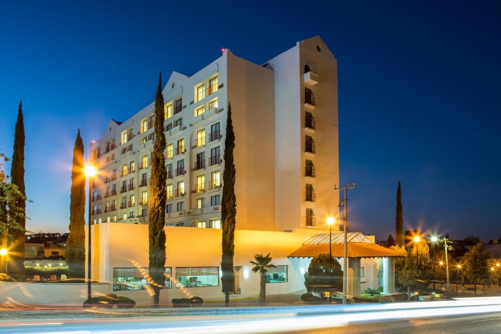 un grand bâtiment avec des arbres devant lui la nuit dans l'établissement Fiesta Inn Chihuahua, à Chihuahua