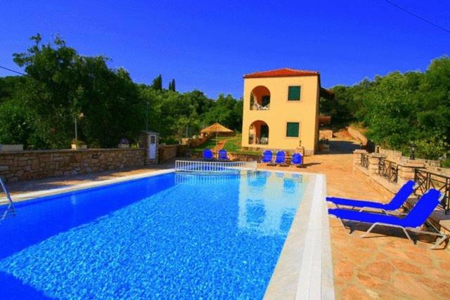 une piscine avec des chaises bleues et une maison dans l'établissement Emily's Apartments, à Kassiopi