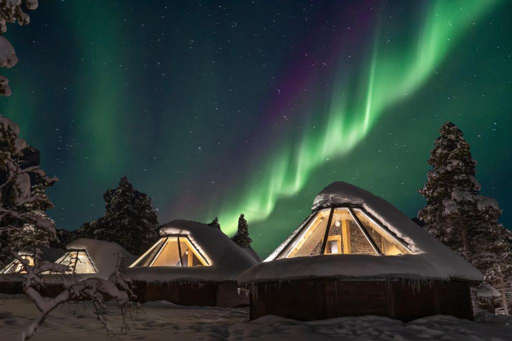 un'aurora su una fila di yurta ricoperta di neve di Wilderness Hotel Muotka & Igloos a Saariselka