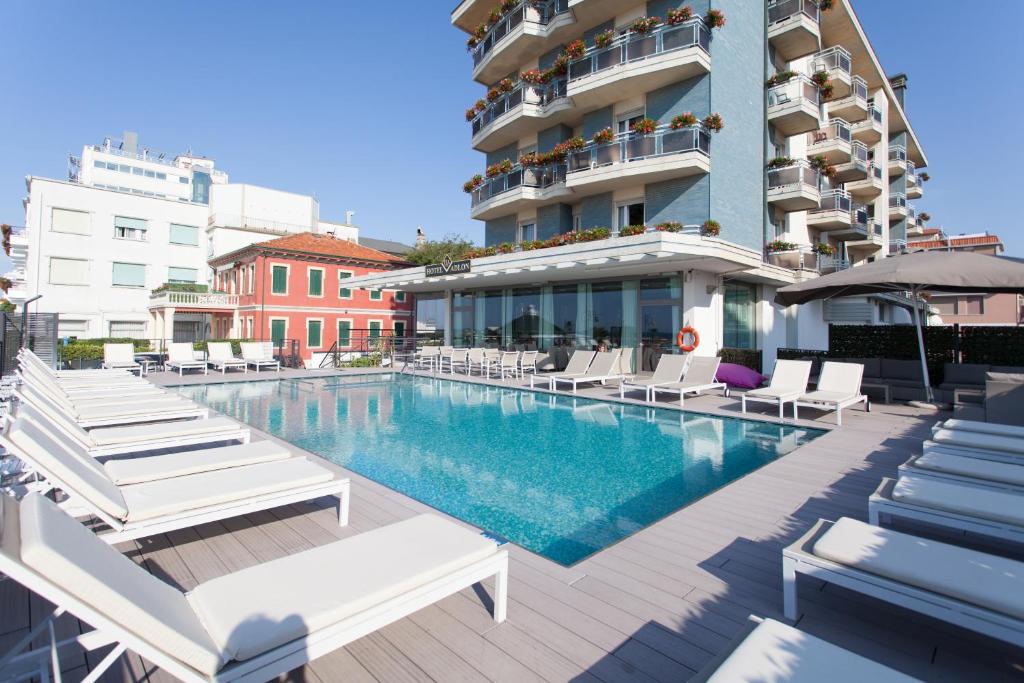 een zwembad met ligstoelen en een gebouw bij Hotel Adlon in Lido di Jesolo