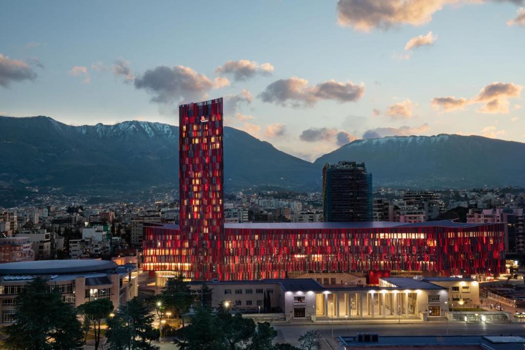 Tirana Marriott Hotel في تيرانا: مبنى طويل مع أضواء حمراء أمام المدينة