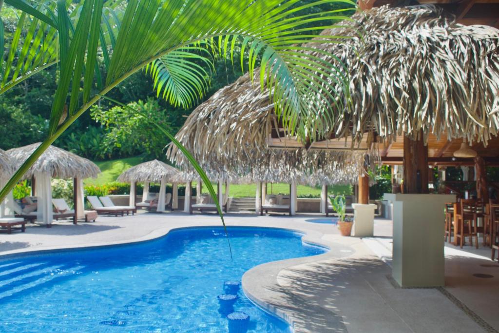 - une piscine avec un parasol et des chaises en paille dans l'établissement Hotel Playa Espadilla & Gardens, à Manuel Antonio