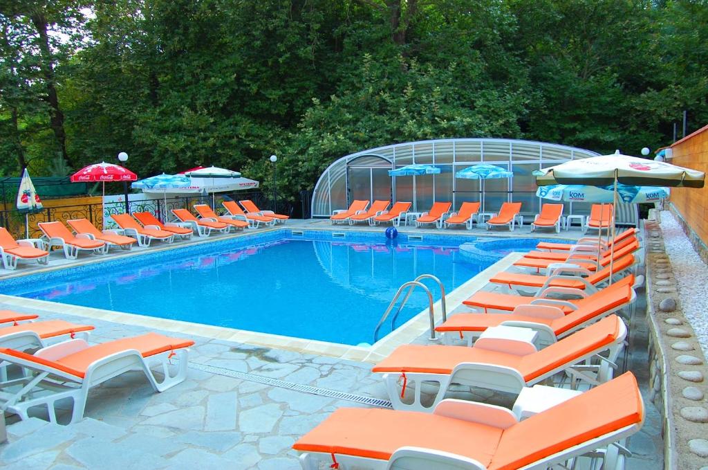 een zwembad met oranje en witte stoelen en parasols bij Family Prim Hotel in Sandanski