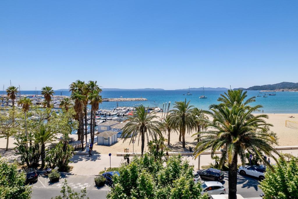 vistas a una playa con palmeras y al océano en Hotel Espadon bleu en Le Lavandou