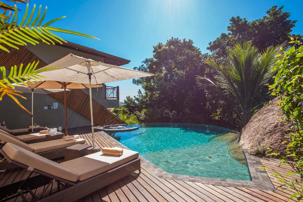 a swimming pool with lounge chairs and an umbrella at Hotel Vila Kebaya in Ilhabela