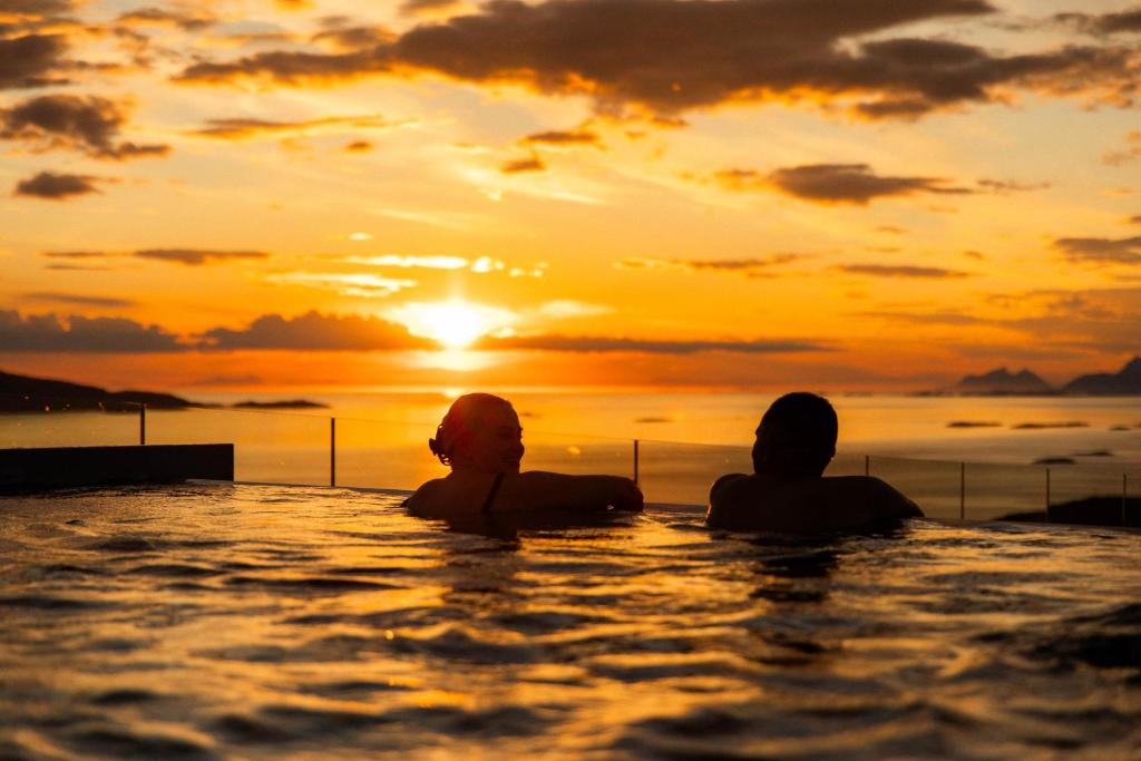 Dos personas sentadas en una piscina infinita viendo la puesta de sol en Wood Hotel Bodø en Bodø