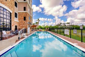 Staybridge Suites - Fort Lauderdale Airport - West, an IHG Hotel في ديفي: مسبح في فندق فيه كراسي ومبنى