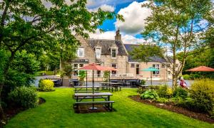 un jardín con mesas de picnic y sombrillas frente a una casa en Pinehurst Lodge Hotel - Aberdeen, en Dyce