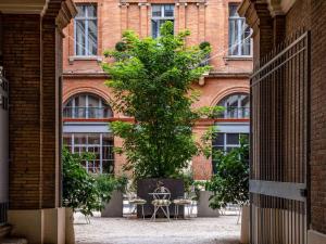 un arbre devant un bâtiment avec des tables et des chaises dans l'établissement Ibis Styles Toulouse Capitole, à Toulouse