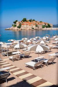 un montón de sillas y sombrillas en una playa en Hotel California by Aycon en Sveti Stefan