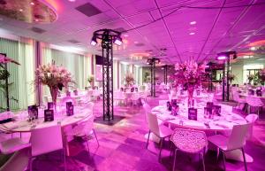 un salón de banquetes con mesas y sillas blancas e iluminación púrpura en Mainport Hotel Rotterdam, a Hilton Affiliate Hotel, en Róterdam