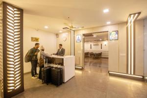 two men standing at a counter in a lobby with luggage at Airport Hotel Chanakya in New Delhi