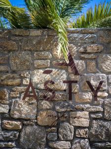 ein Schild an einer Steinmauer mit einer Palme in der Unterkunft Asty Mykonos Hotel & Spa - World of One Hotel Group in Mykonos Stadt