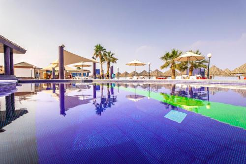 una piscina in un resort con palme e ombrelloni di Royal Beach Hotel & Resort a Dibba