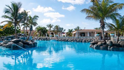 una piscina en un complejo con agua azul y palmeras en Palm Oasis Maspalomas en Maspalomas