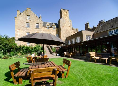 Dornoch Castle Hotel في دورنوش: طاولة وكراسي مع مظلة أمام المبنى