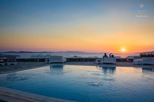 zwei Personen, die bei Sonnenuntergang auf Stühlen am Pool sitzen in der Unterkunft Aeolos Resort in Mykonos Stadt