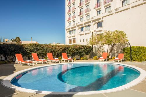 une piscine avec des chaises longues et un bâtiment dans l'établissement Fiesta Inn Chihuahua, à Chihuahua