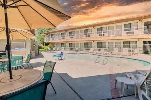 ein Pool in einem Hotel mit Stühlen und einem Sonnenschirm in der Unterkunft The Oakhurst Inn at Yosemite in Oakhurst