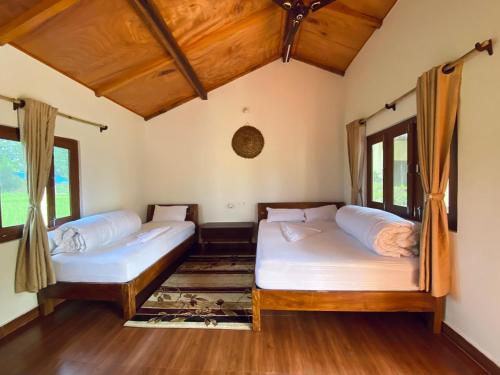 two beds in a room with wooden floors and windows at Bardia Eco Friendly Homestay in Bhurkīā