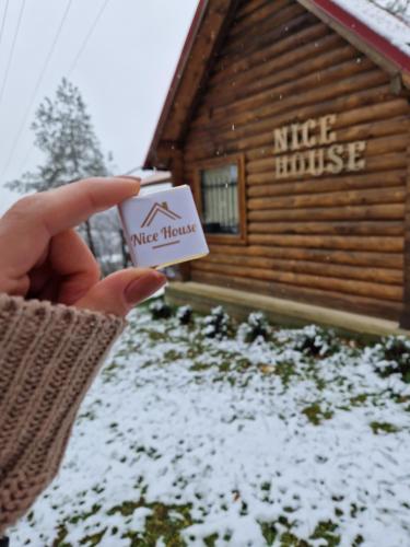 a person holding a mile house card in front of a log cabin at Nice House in Maidan Village