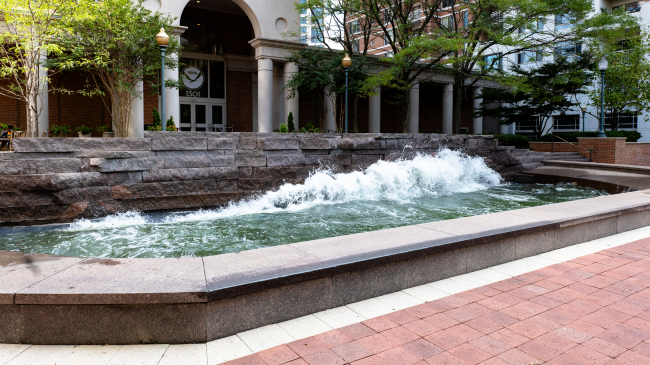 Photo of the “Coastline” wave pool art installation outside NOAA’s Silver Spring, MD campus. Waves crash against a rough stone wall in a long rectangular pool.