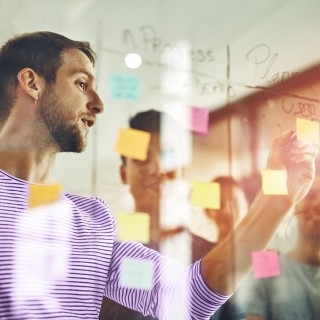 Image of man making notes in clear board in front of teammates