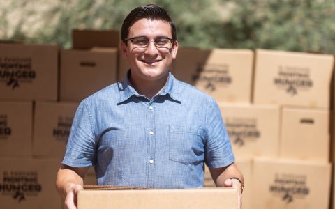 A smiling young man standing in front of many food boxes.