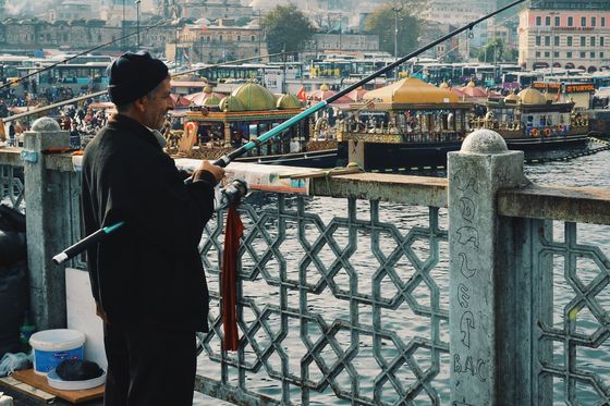 man fishing on a bridge in istanbul with the blue mosque in the background