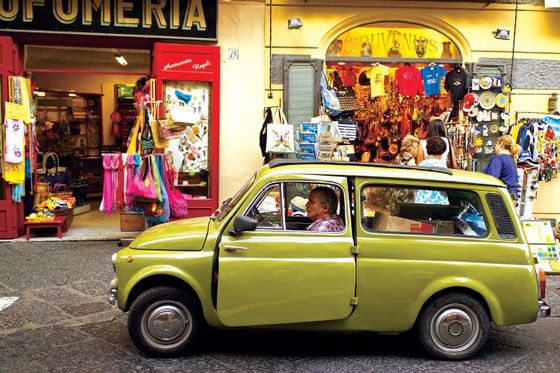 an old green car parked in front of a store in italy