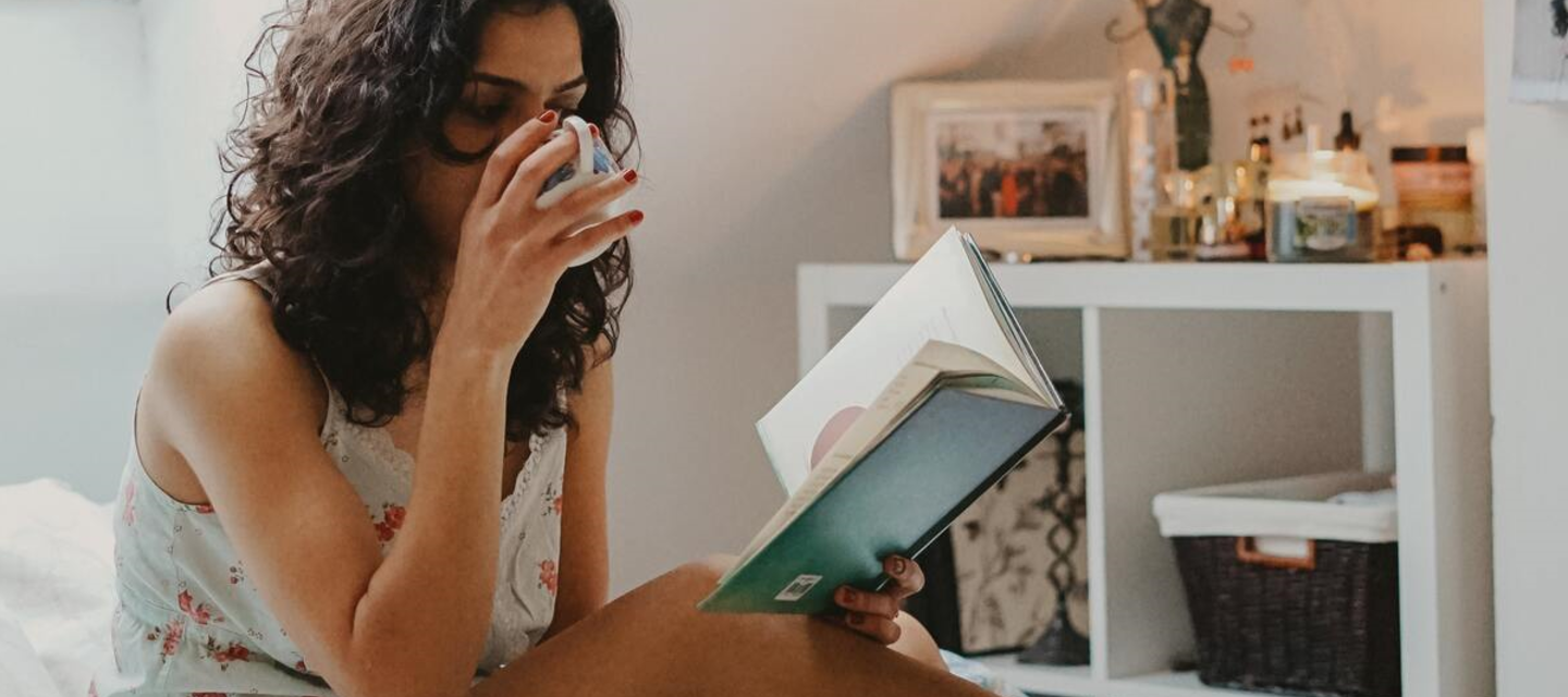 Woman reading a book and drinking coffee in bed