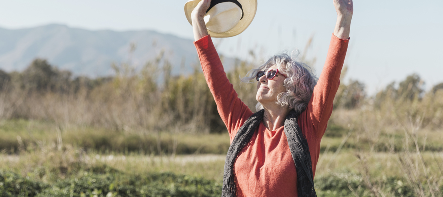 An older woman raising her hands in a happy gesture in the nature