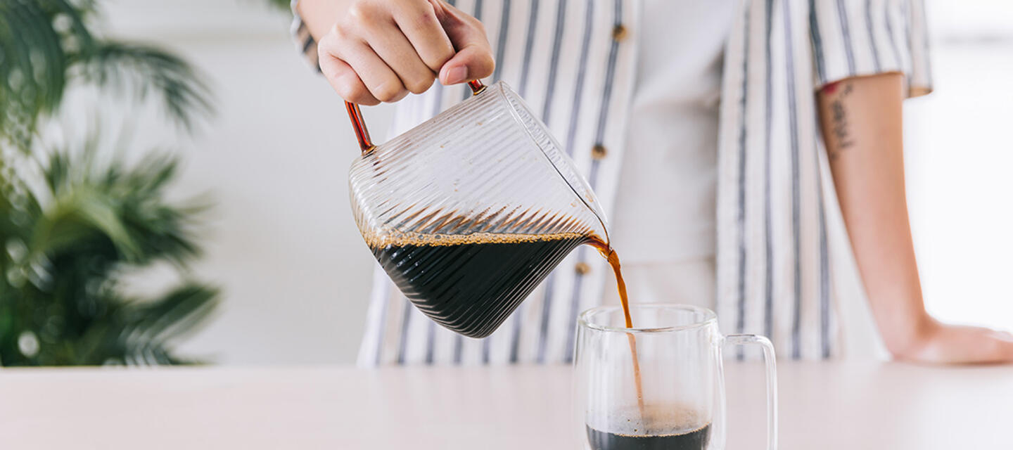 Closeup of a barista pouring coffee from a glass jug to a glass