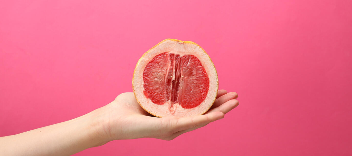 Female hand holding half of grapefruit on pink background