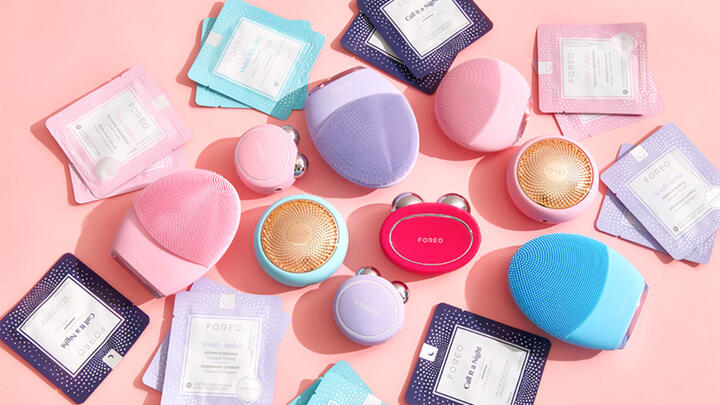 A stash of colorful FOREO facial devices and products on a pink surface