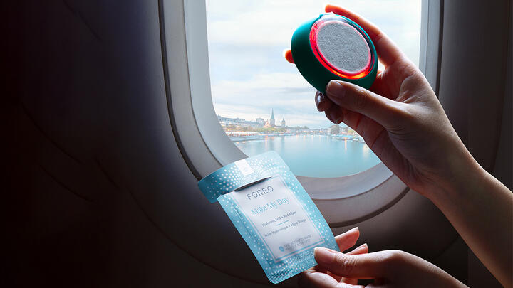 Hands holding FOREO UFO 3 device by an airplane window