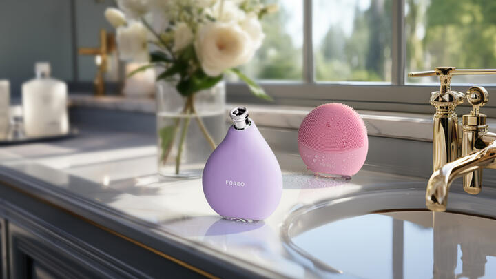 FOREO KIWI derma and LUNA 4 mini on a marble counter in a bathroom, a vase with white flowers in the background