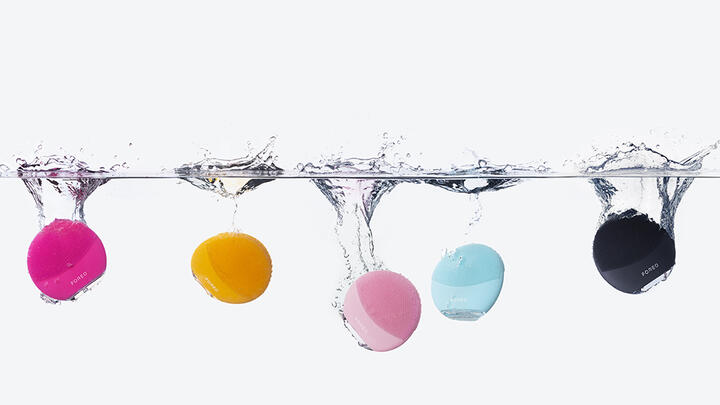 Colorful FOREO LUNA facial brushes falling into water