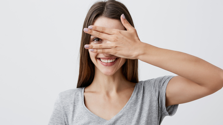 Young woman hiding her face behind the palm of her hand, smiling