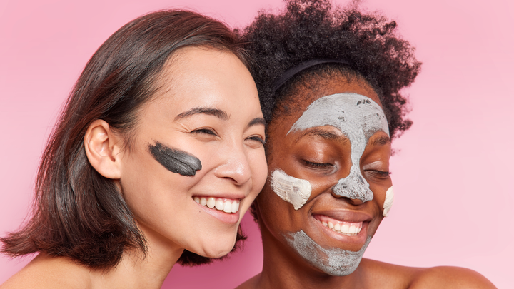 Two women smiling with clay masks on their faces