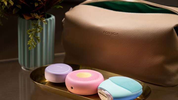 FOREO skincare devices in front of a brown Bon Voy toiletry bag