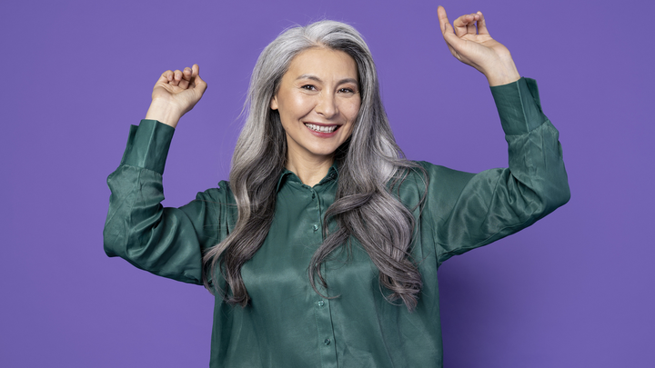 Happy woman with long grey hair in a dark green shirt in front of a purple background