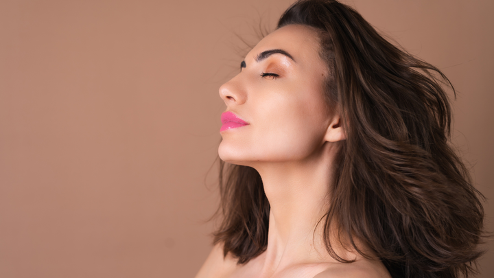 A woman with thick wavy hair with her eyes closed against a brown background